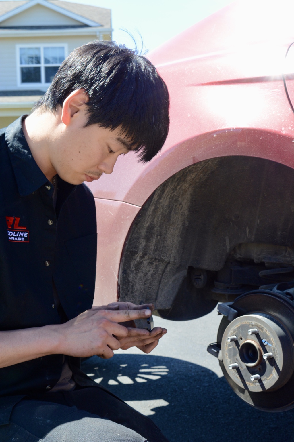 Ryan inspecting a brake component beside a red vehicle